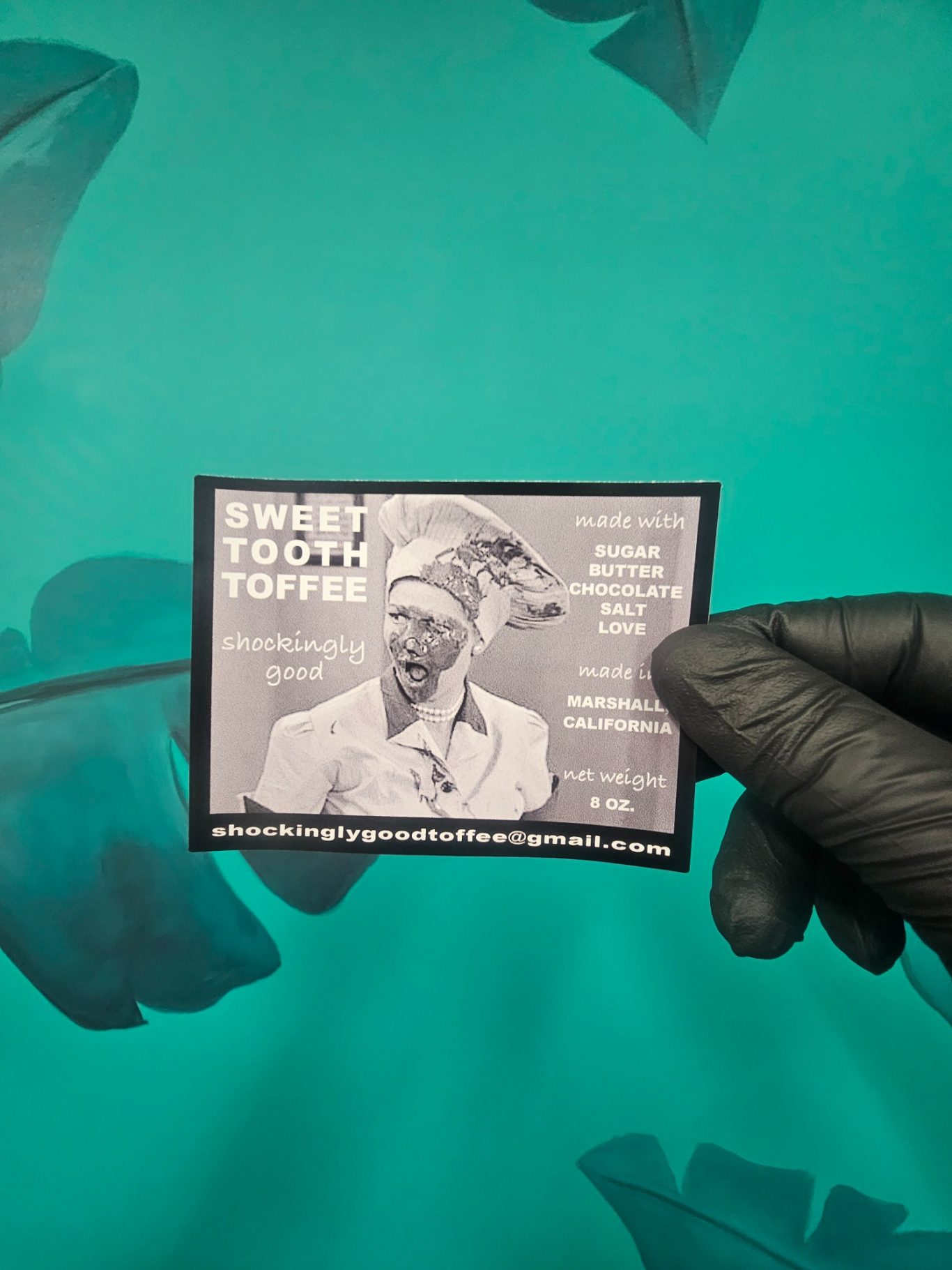 Hand holding a coffee card featuring a woman in a white suit against a teal background.